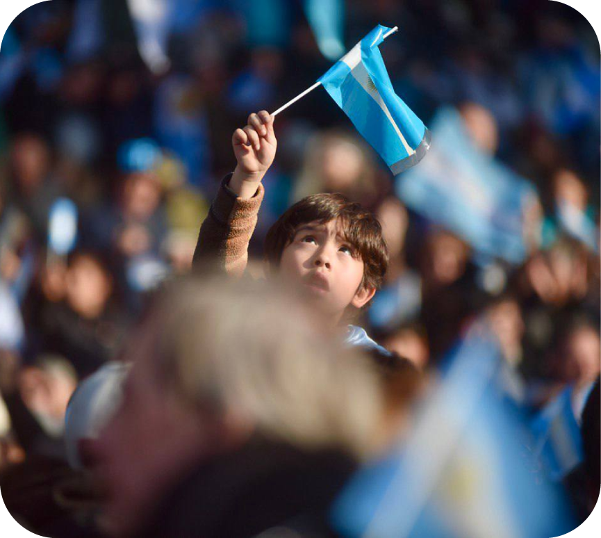 Foto de un niño agitando una bandera Argentina entre una multitud.